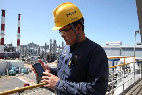 한화토탈 직원이 충남 대산 석유화학 공장에서 스마트폰으로 현장 생산설비 점검 결과를 확인하고 있다.  한화토탈 제공